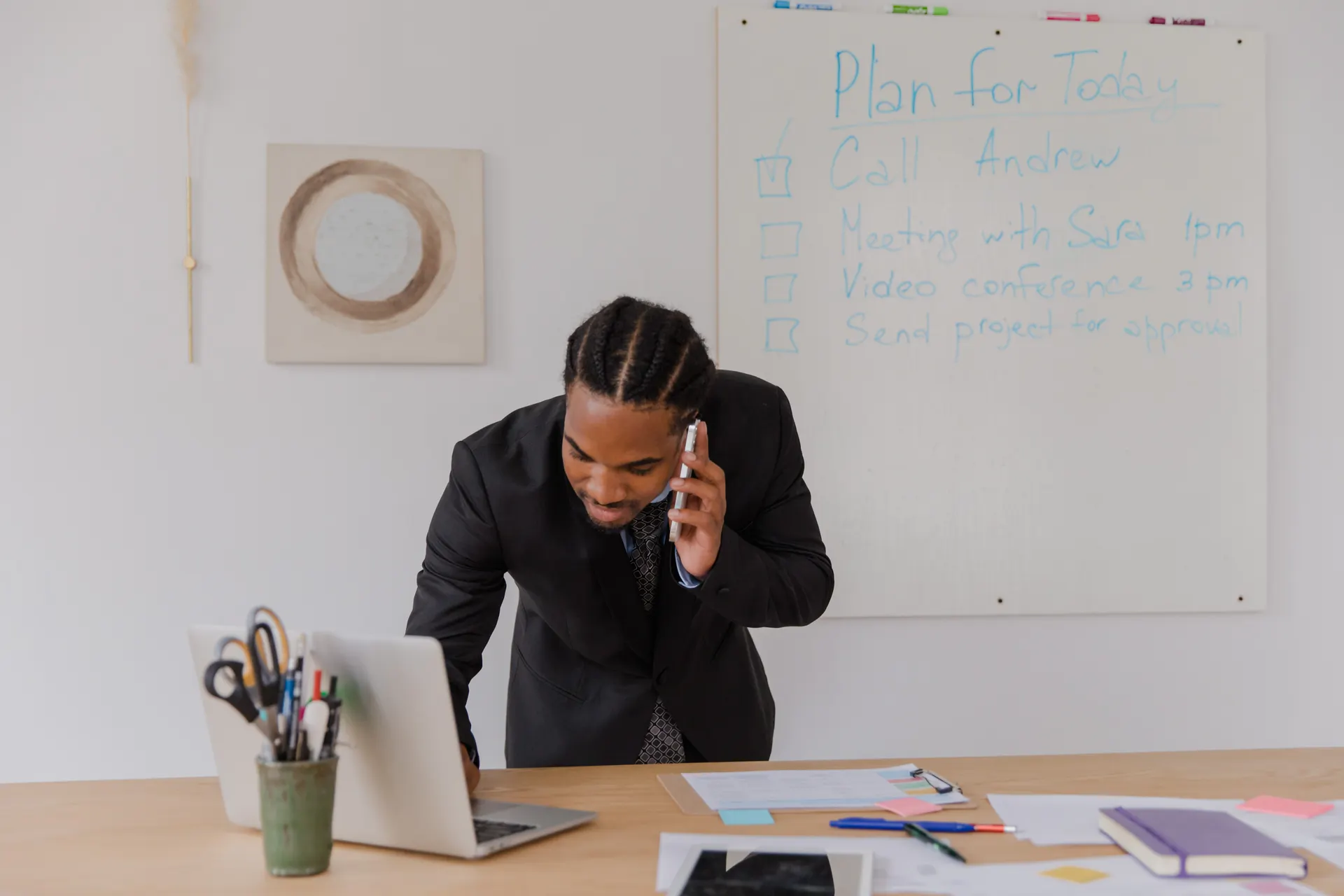 Commercial au téléphone penché sur son bureau, ordinateur portable ouvert, en pleine prise de contact avec un prospect