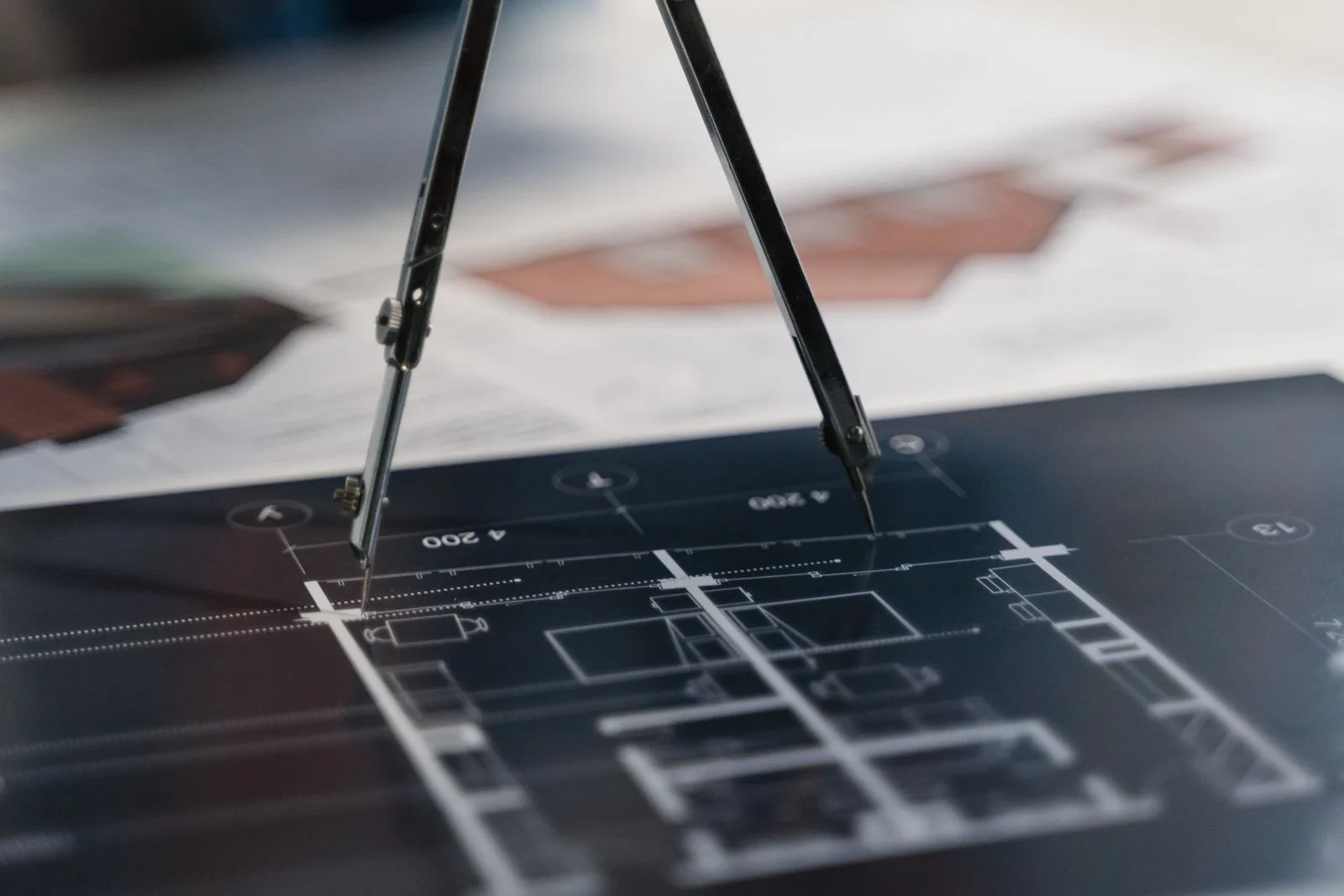 Compas posé sur un plan technique coté, au milieu d'autres documents d'étude