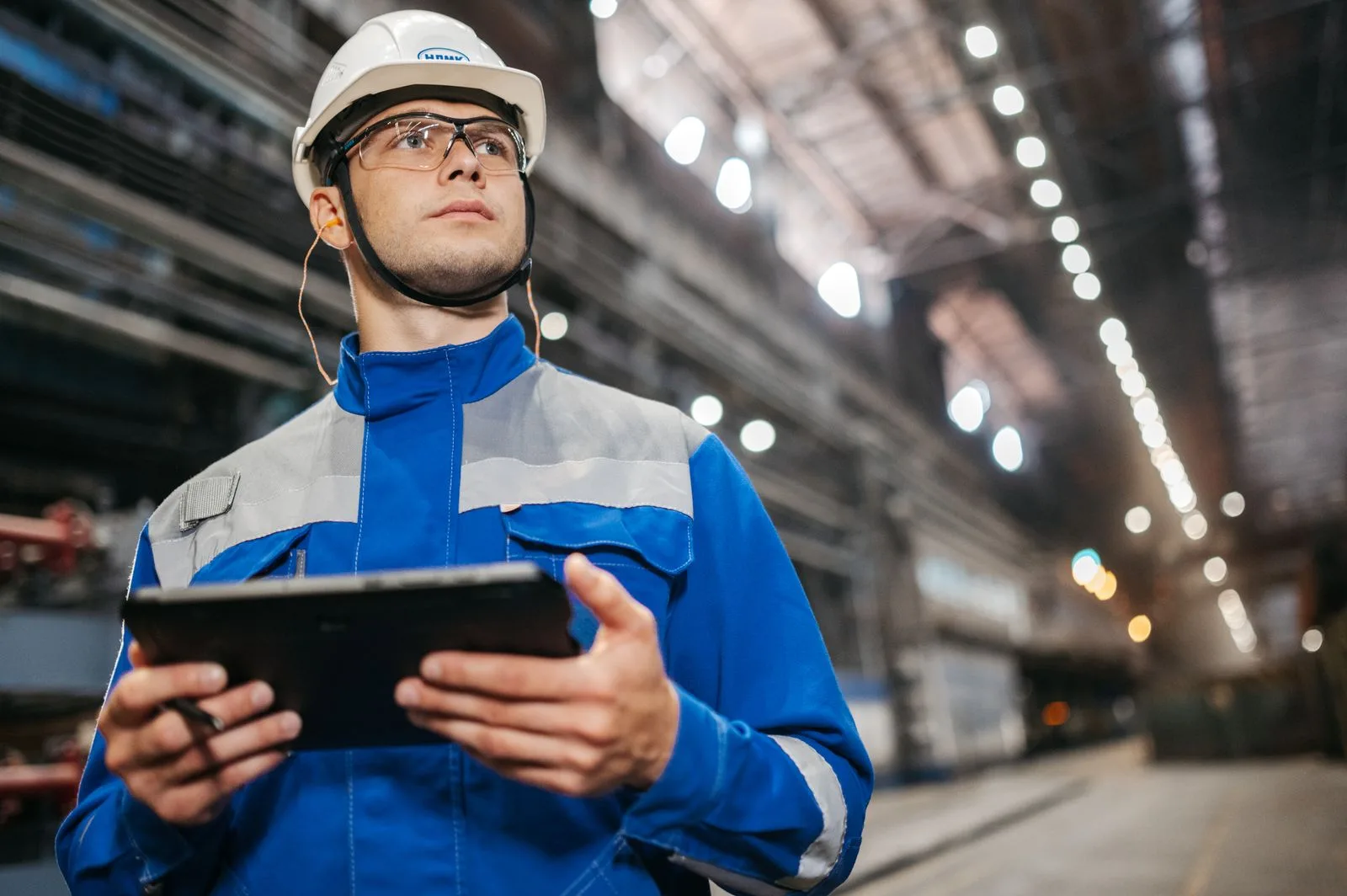 Technicien en tenue de travail consultant une tablette dans un atelier industriel