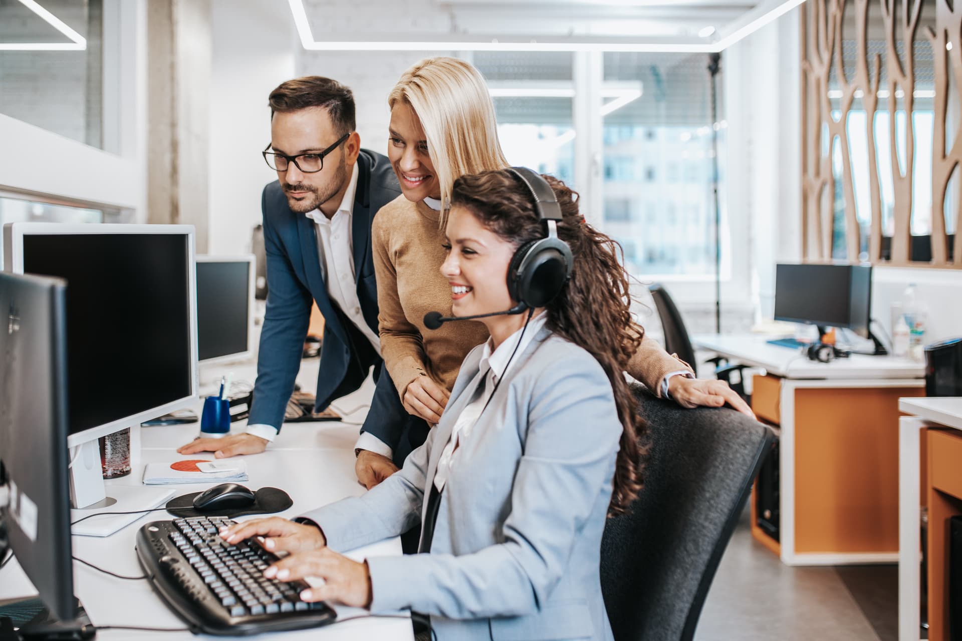 Équipe support entourant une conseillère au casque devant son écran en open space