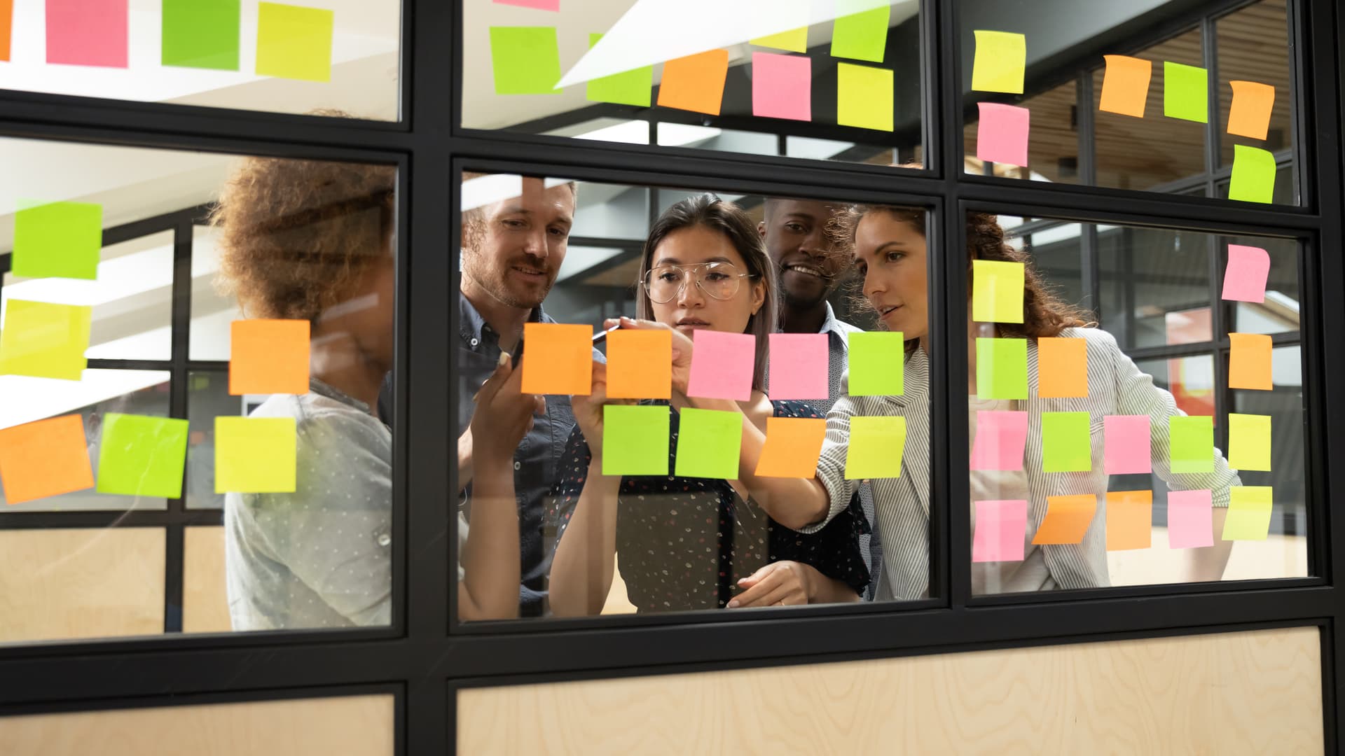 Équipe startup en sprint planning derrière une paroi vitrée couverte de post-its