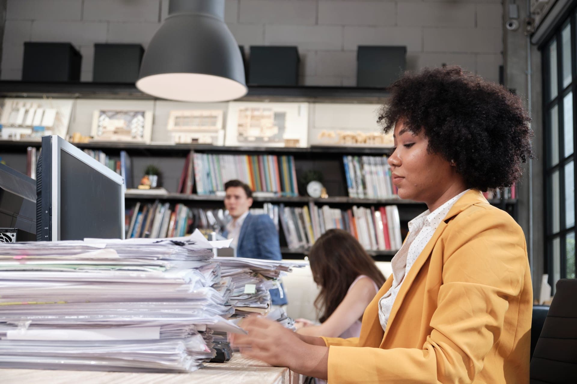 Employée traitant des piles de dossiers papier à son bureau avant leur numérisation